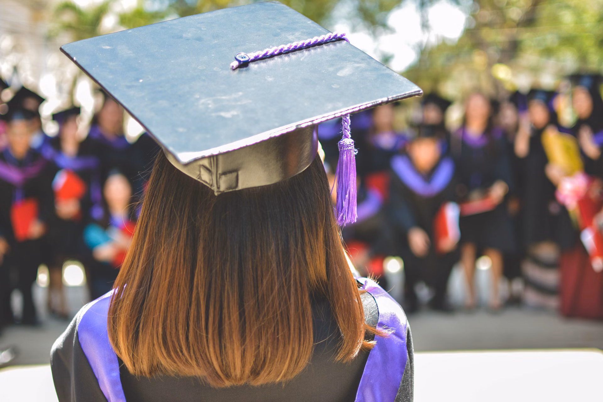  A person wearing a graduation cap and gown is looking out at a crowd of people. The image represents the search query 'An app with a feature for autoinvesting in a childs education savings account'.